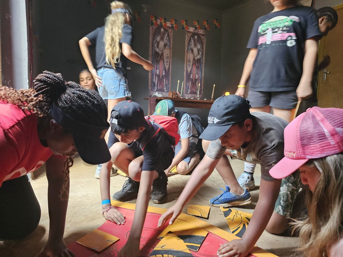 Children crouch on the floor fitting red and yellow puzzle pieces together in a dimly lit themed room