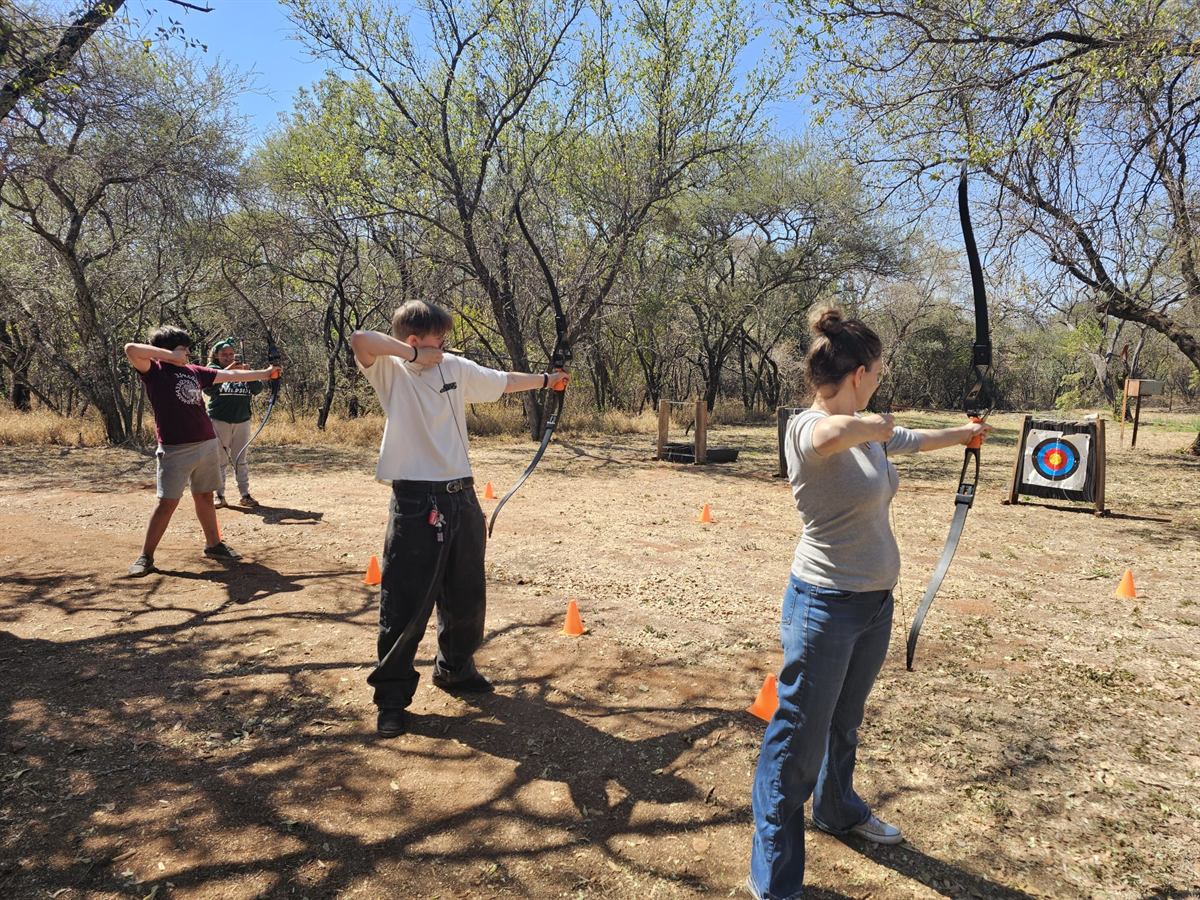 Four archers, including an adult, shooting side by side at targets on a bush archery range