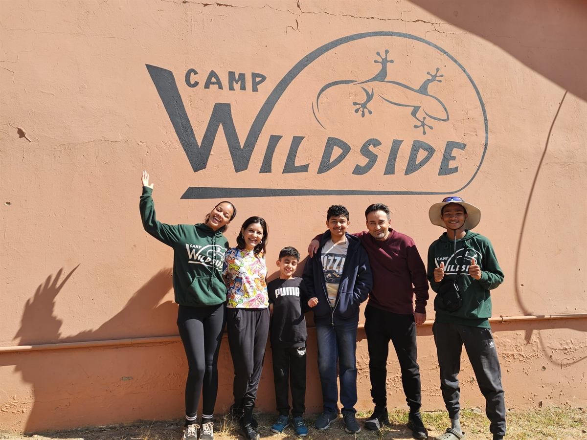 A family with two Camp Wildside staff in front of the painted camp logo wall
