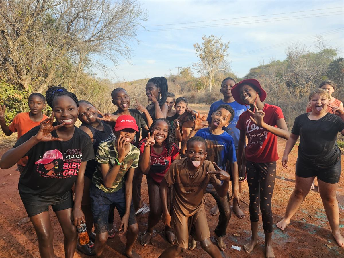 A muddy group of campers pulling faces on a red dirt road after the obstacle course