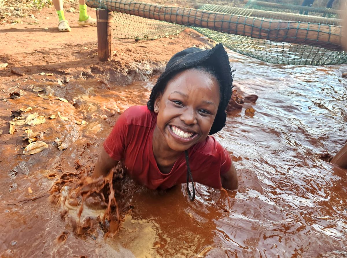 A girl chest-deep in the muddy water trench under the cargo net, splashing and smiling