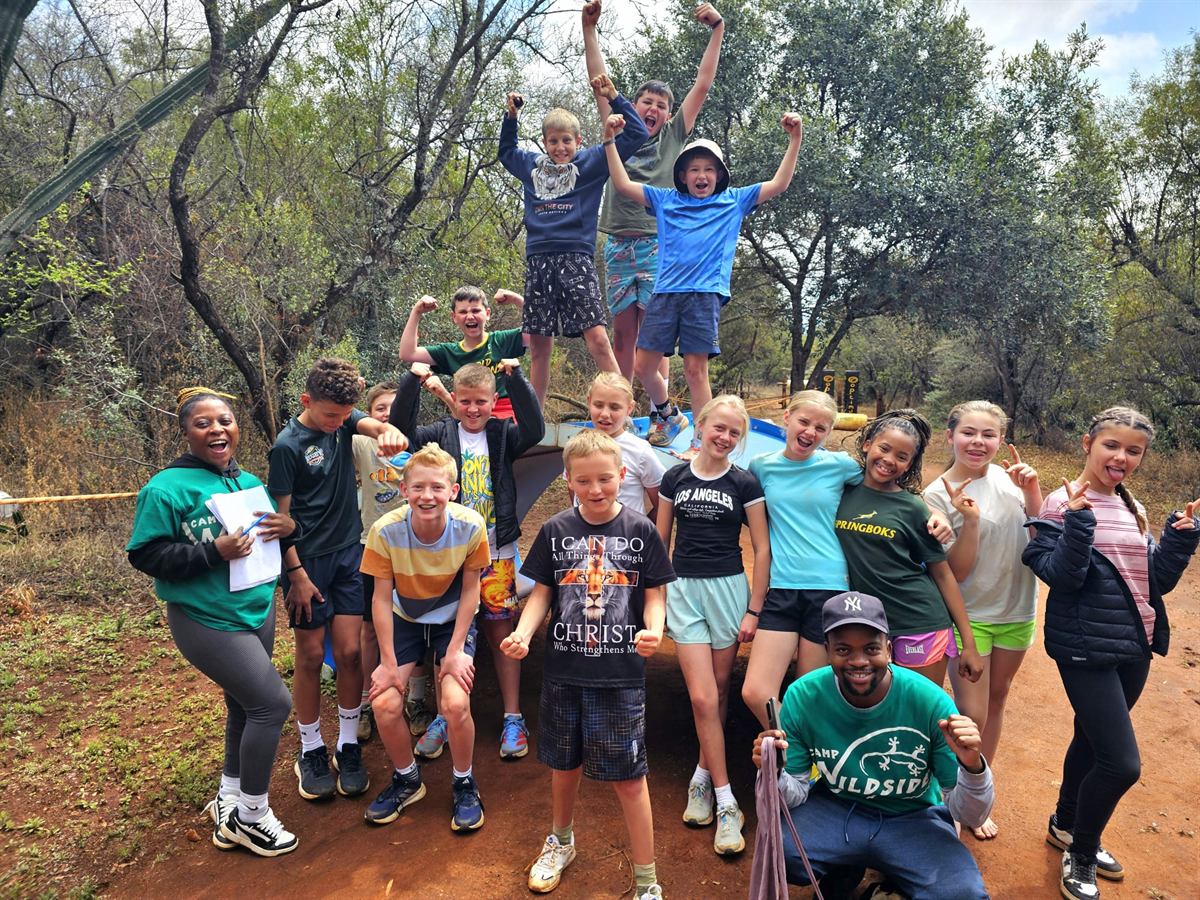 Campers with fists raised standing in and around a blue boat in the bush, two counsellors alongside