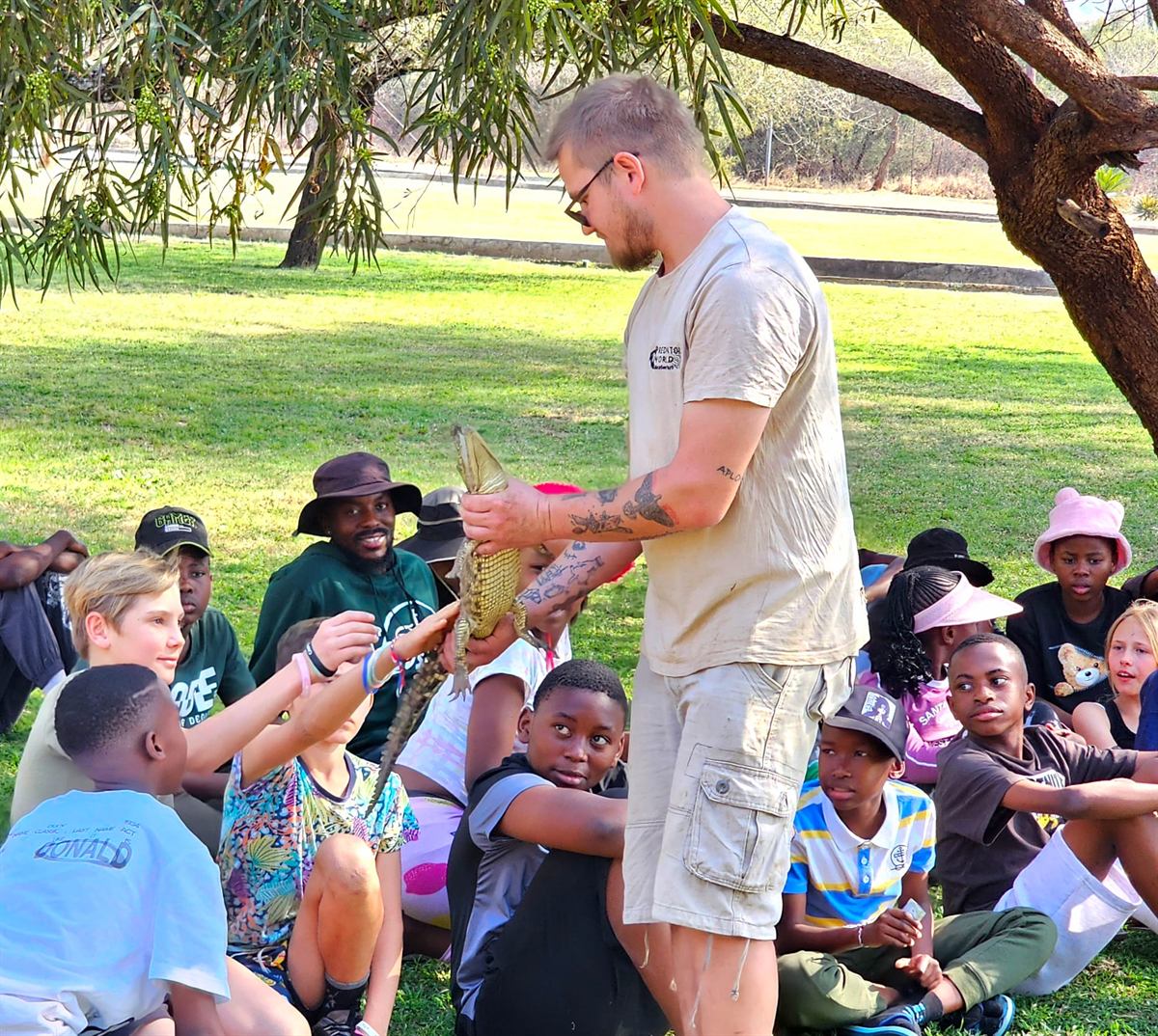 Campers reach to touch a small crocodile held by the handler during the reptile show