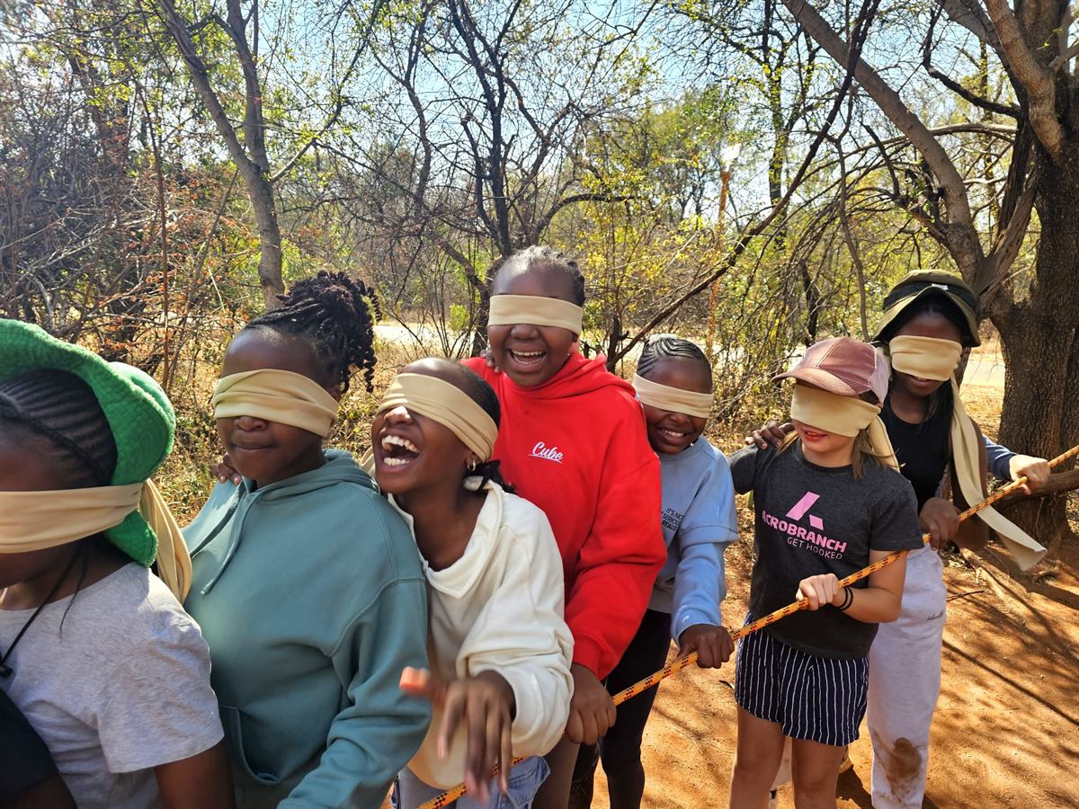 Blindfolded children laughing together while holding a guide rope among winter trees