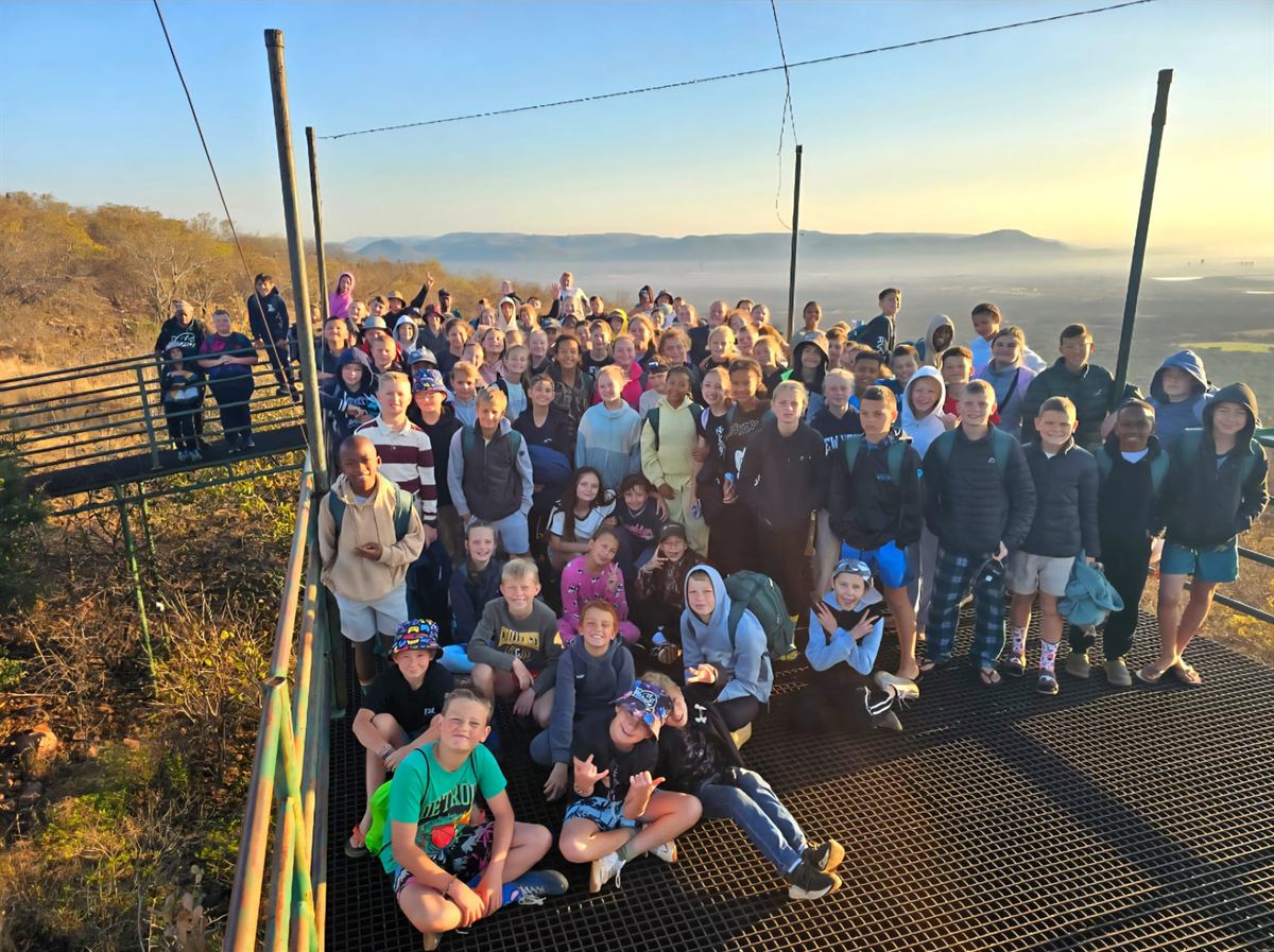 A large group of campers gathered on the railed lookout platform, hazy valley and hills behind
