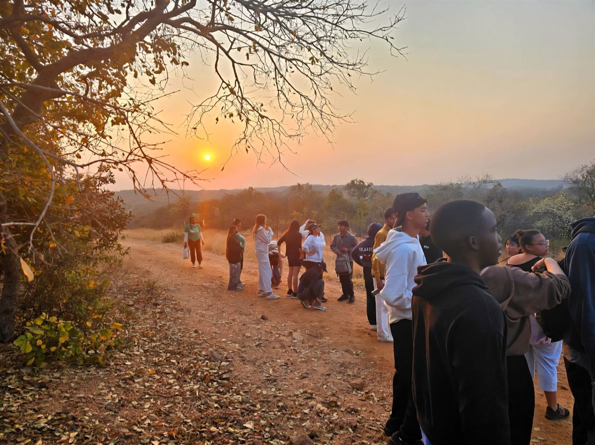 Teenagers on a red dirt track through the bush with the sun low over the trees
