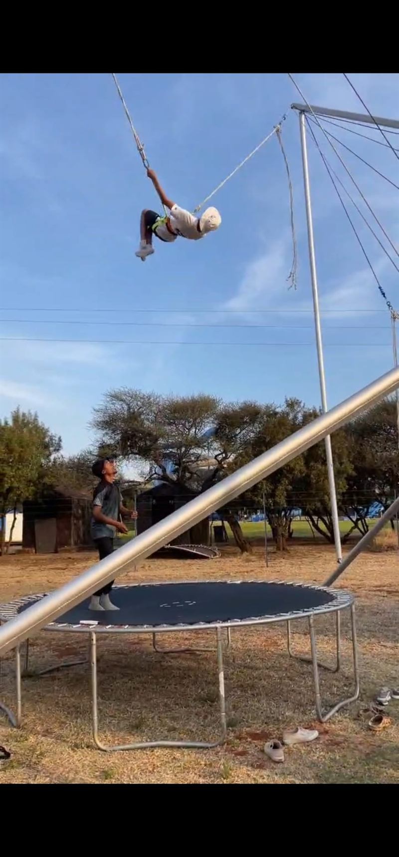 A camper flies high on the bungee trampoline beside the waterpark, a counsellor watching from below