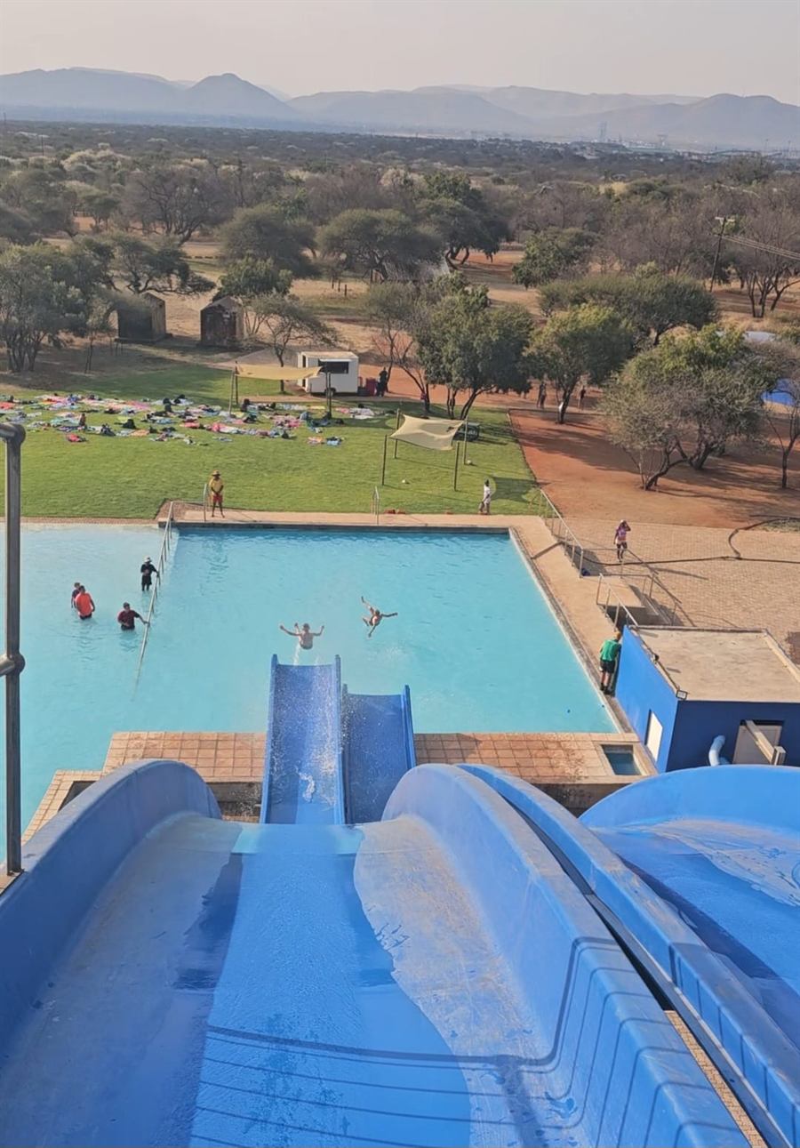 Looking down the blue slide into the pool, campers on the lawn and the bushveld beyond