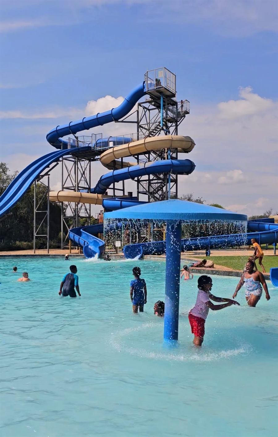 Children playing in the shallow pool under the mushroom fountain, the slide tower behind them